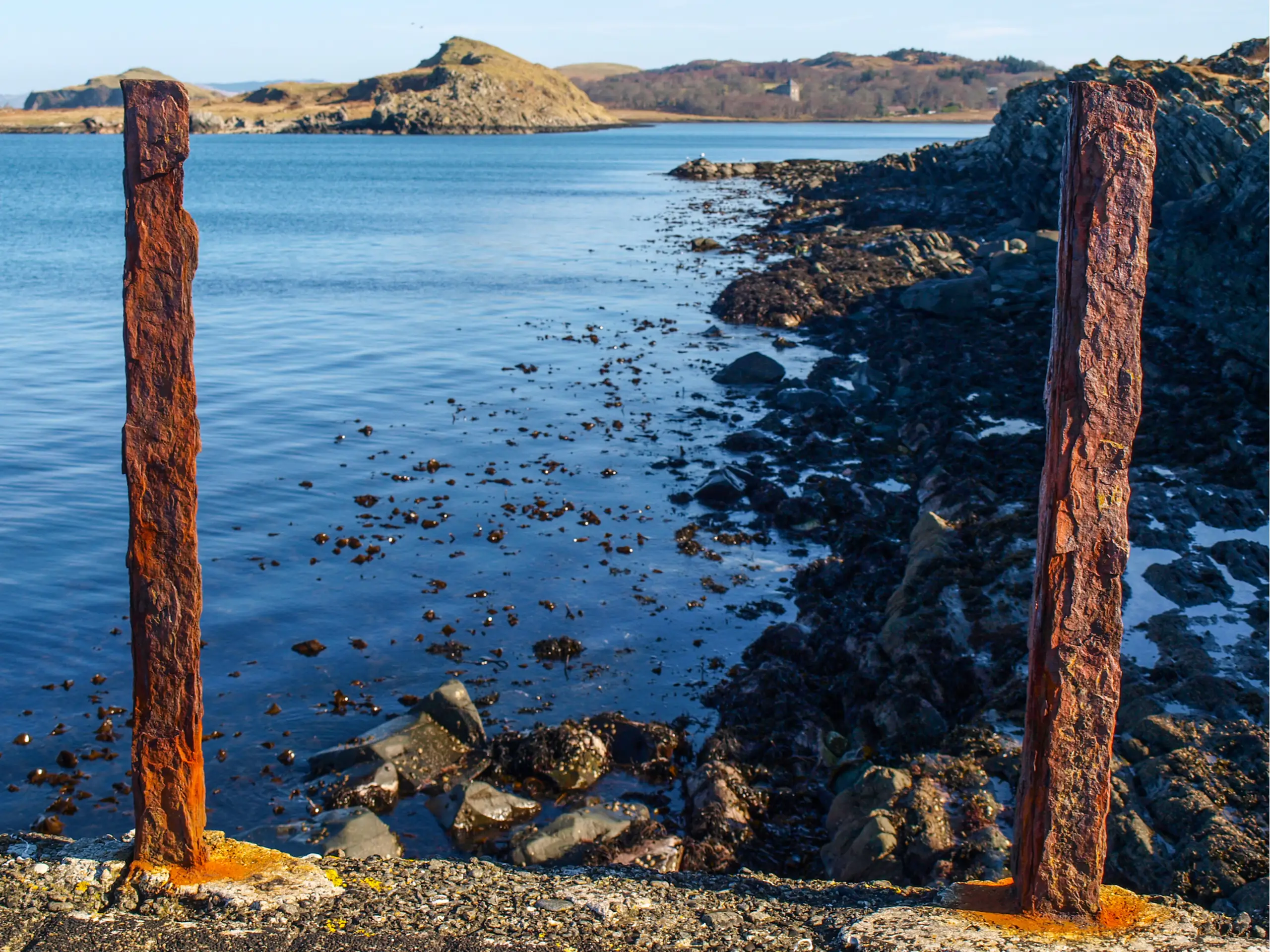 Rusting posts on an ancient pier, the castle in the distance